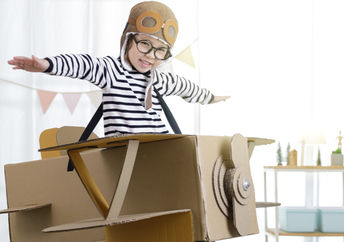 Creative little girl uses her imagination as she ‘flies’ in a cardboard box.