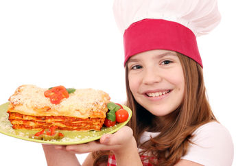 A smiling young girl is holding a plate of lasagna.