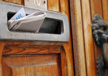 Mailbox filled with rolled spam newspaper in an old wooden door.