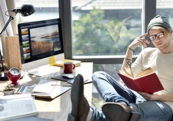 Man engrossed in reading a book at his workstation.