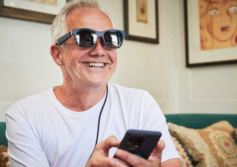 A man smiles as he wears augmented reality glasses, seeing subtitles of a conversation.
