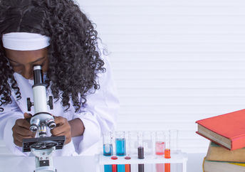 Young girl studying science and using microscope in classroom at school