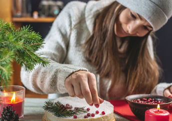 A woman decorating a festive cake with red berries.