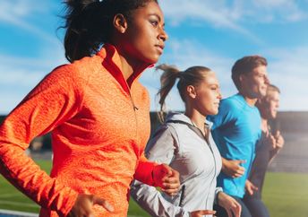 Young woman running with her team in a stadium.