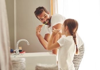 Father and daughter brushing their teeth.