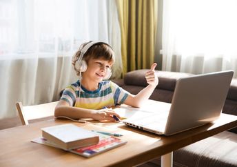 A boy wearing headphones gives a thumbs-up while using his laptop.