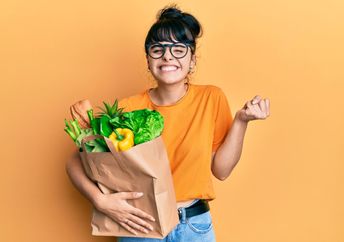 A woman smiles and holds a bag filled with food.