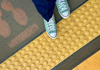 A woman walking on a yellow blind path for partially-sighted pedestrians.