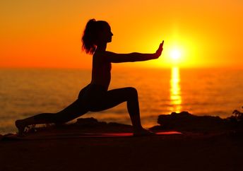 A woman does Tai Chi at sunset on the beach.