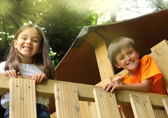 Smiling children look out from a wooden treehouse.