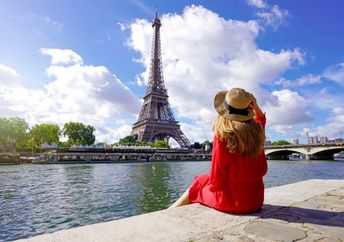 A woman sits on the quay of the Seine River looking at the Paris landmark Eiffel Tower.