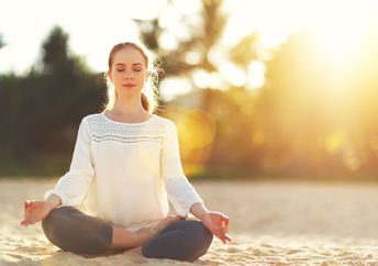 A woman practices yoga and meditates on the beach.
