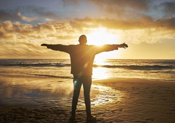 A silhouette of a man at the beach standing with his arms raised.