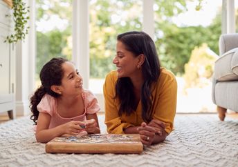 A mother and daughter lie on the floor at home.