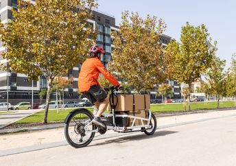 A young courier with a helmet rides a cargo bike.