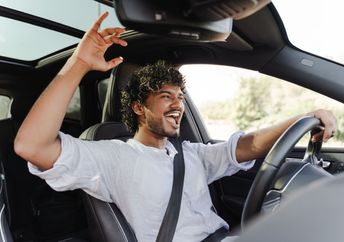 A young man happily drives while singing to music.