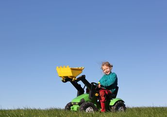 A happy young girl plays on a toy tractor.