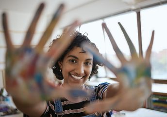 A woman smiles with colorful painted hands.