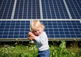 Child playing with a piggy bank in front of solar panels.