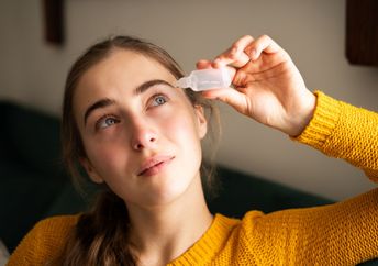 A woman using eye drops in a living room.