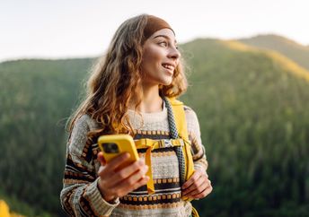A woman walks in nature while holding her phone.