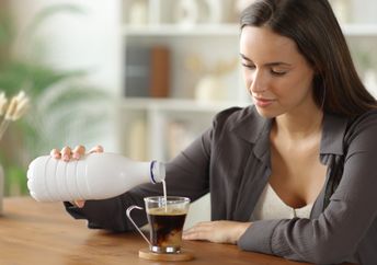 Woman adding milk to her coffee.