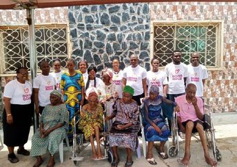 Good Deeds Day volunteers in Nigeria stand behind elderly residents seated outdoors.