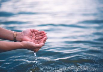 Two hands touch blue water.