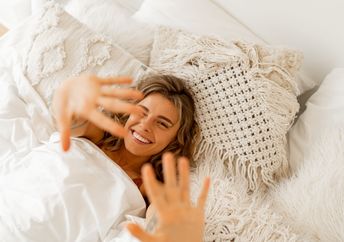 A woman lies in a white cozy bed.