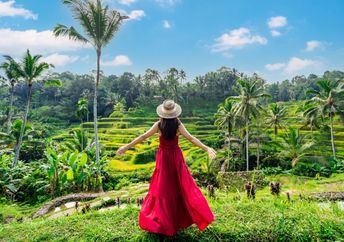 A female tourist in a red dress looks at a rice terrace in Bali, Indonesia.