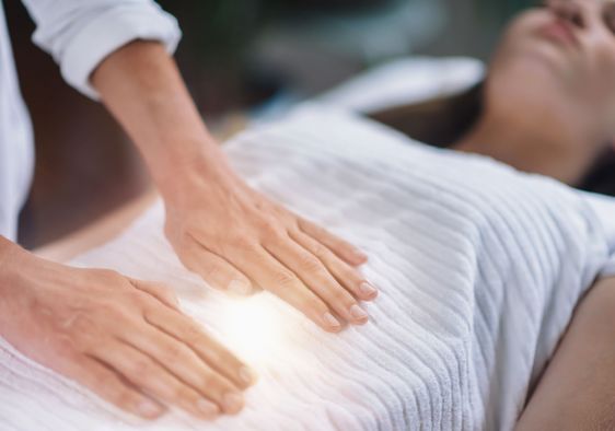 A woman during an energy healing session as a practitioner places hands gently on her upper body.