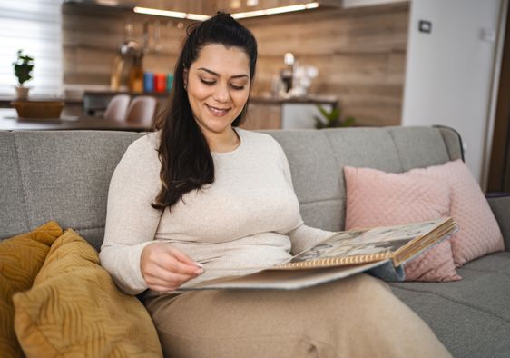 A woman looking at a photo album while sitting on a couch.