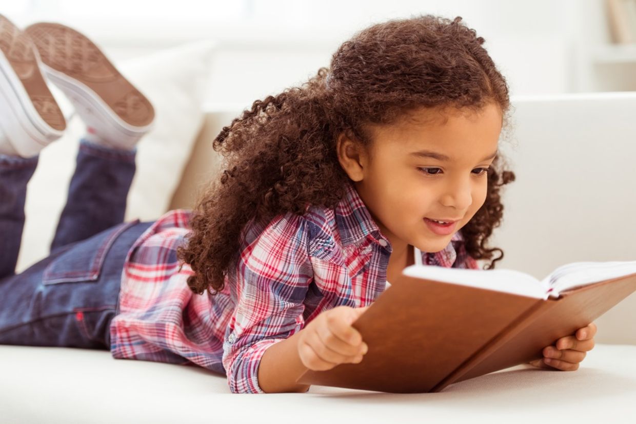 Young girl with curly hair reading a book on the floor