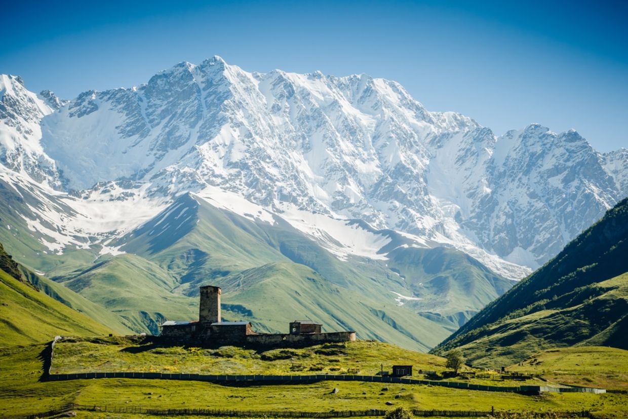 View of Ushguli village and grand ridges that lights up. Location Lamaria Church Jgrag, Upper Svaneti, Georgia, Europe. Main Caucasian Ridge.