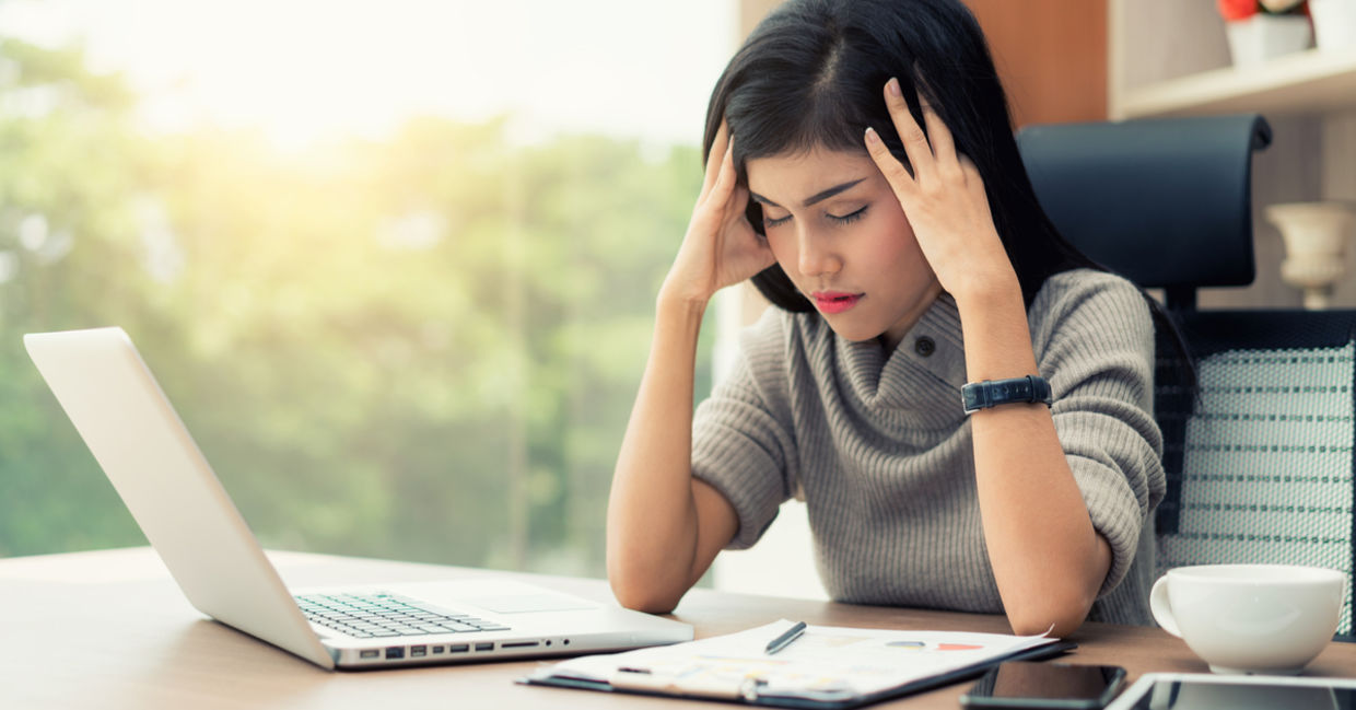 A young woman sits at her desk with a headache