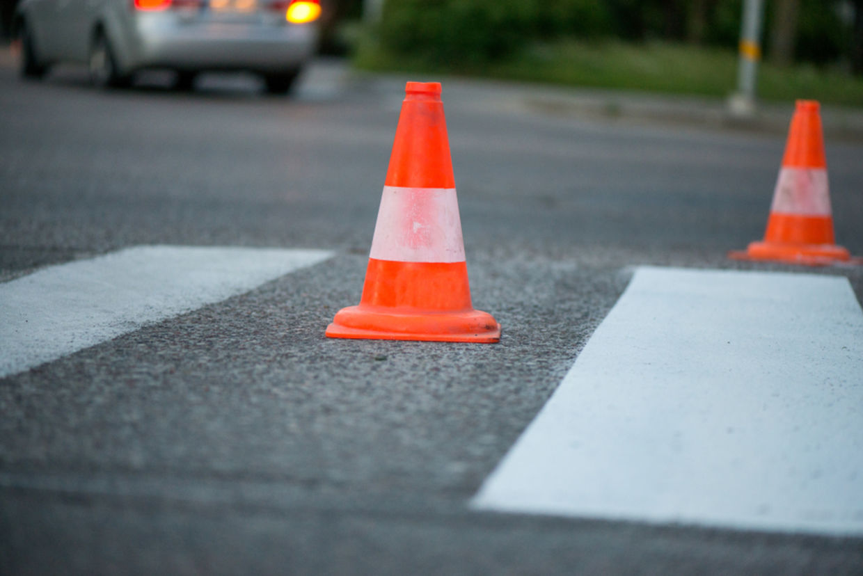 Macro shot of road traffic cones with orange and white stripes standing on street on gray asphalt during road construction works. Just painted white street lines on pedestrian crossing