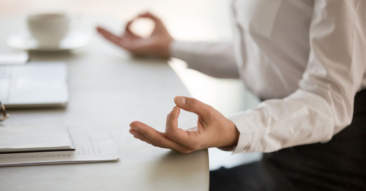 A man practices mindfulness at work by meditating at his desk.