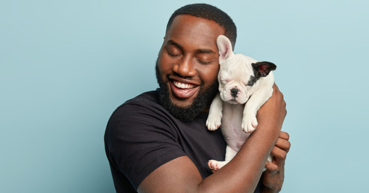 A joyful man hugs his French bulldog puppy.