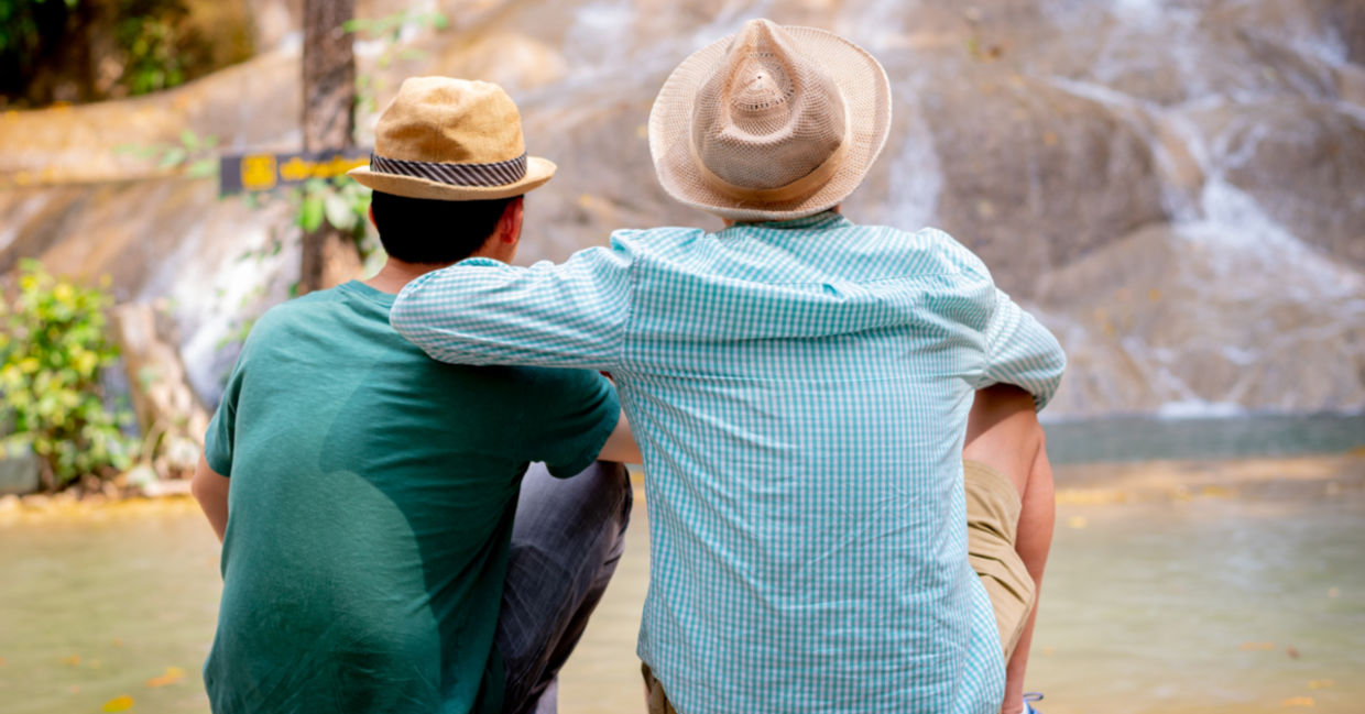 Two good friends enjoy each other’s company as they sit in front of a waterfall.