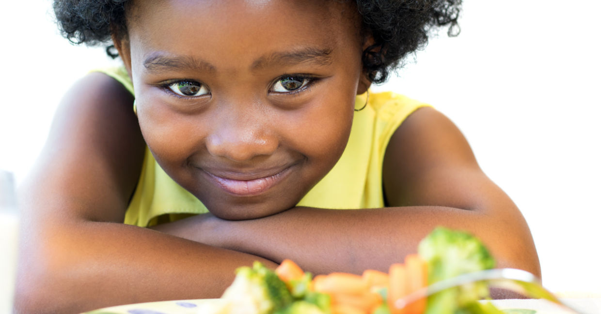A young girl with a plate of healthy food smiles.