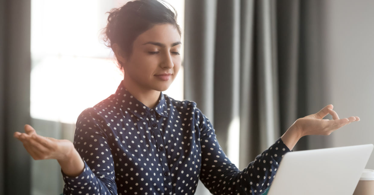 A businesswoman takes time out to meditate at her desk.