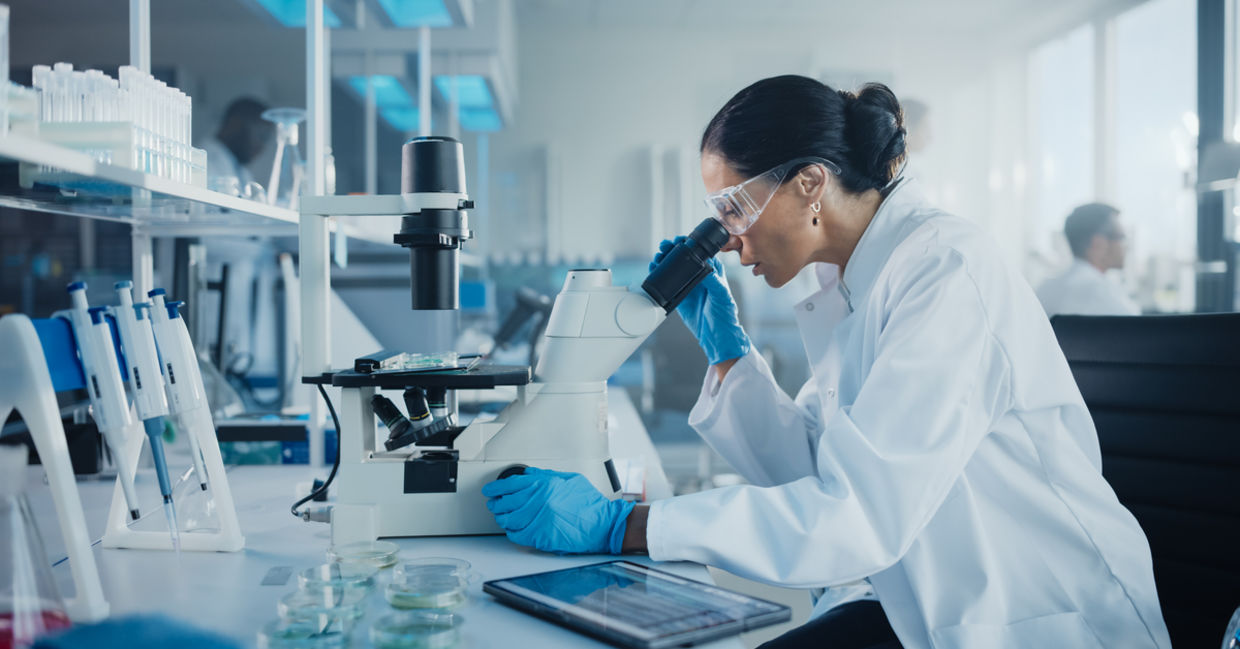 Female scientist in a lab looking under a microscope.