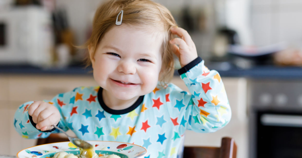Happy girl eating chicken noodle soup made with a healthy recipe for kids.