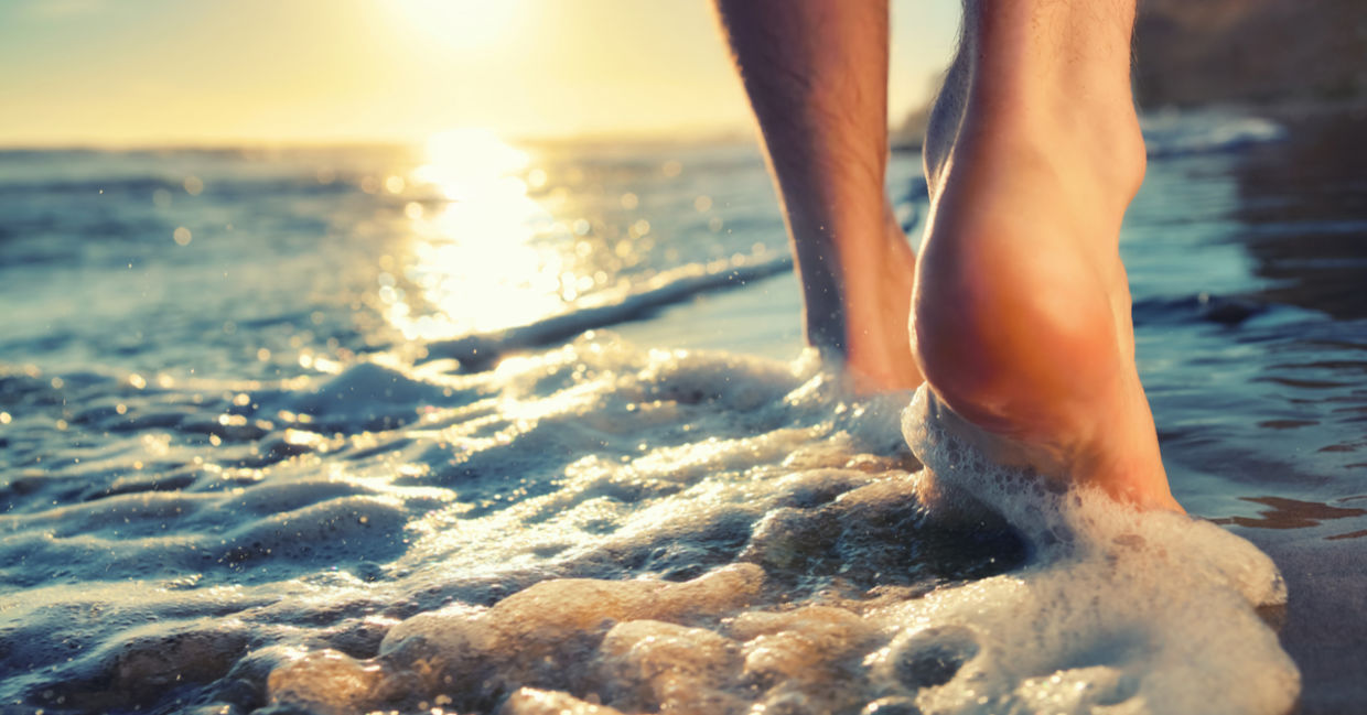 A man takes a sunset walk, barefoot, in the foaming waves.
