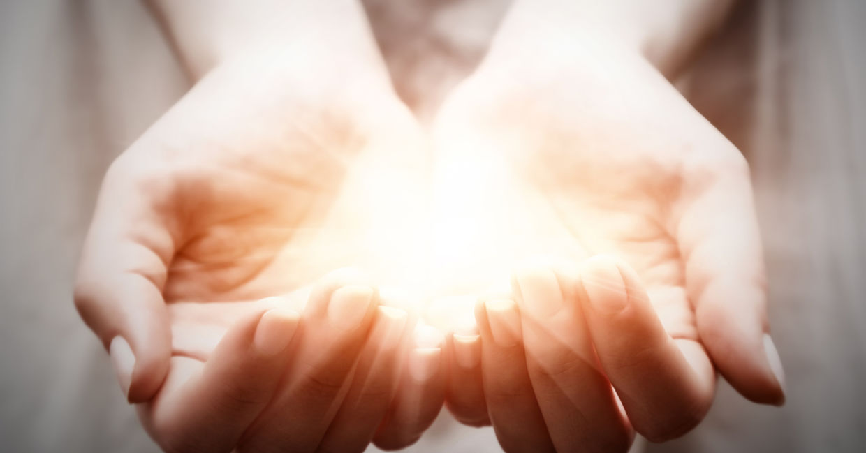A woman cups light in her palms, representing giving and spirituality.