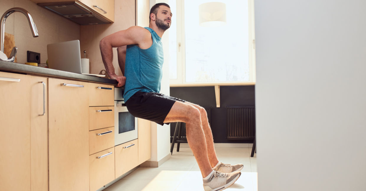 A young man exercising using the kitchen counter.