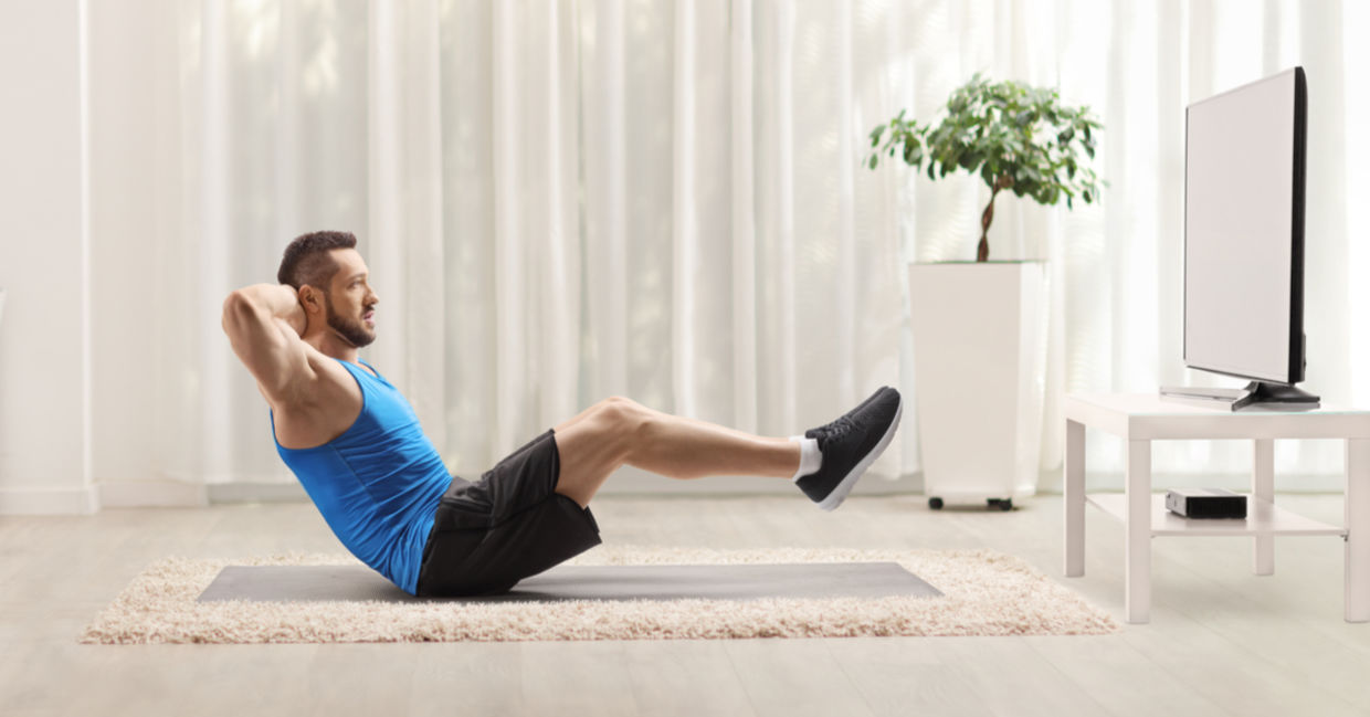 A man is doing sit ups in front of the TV.