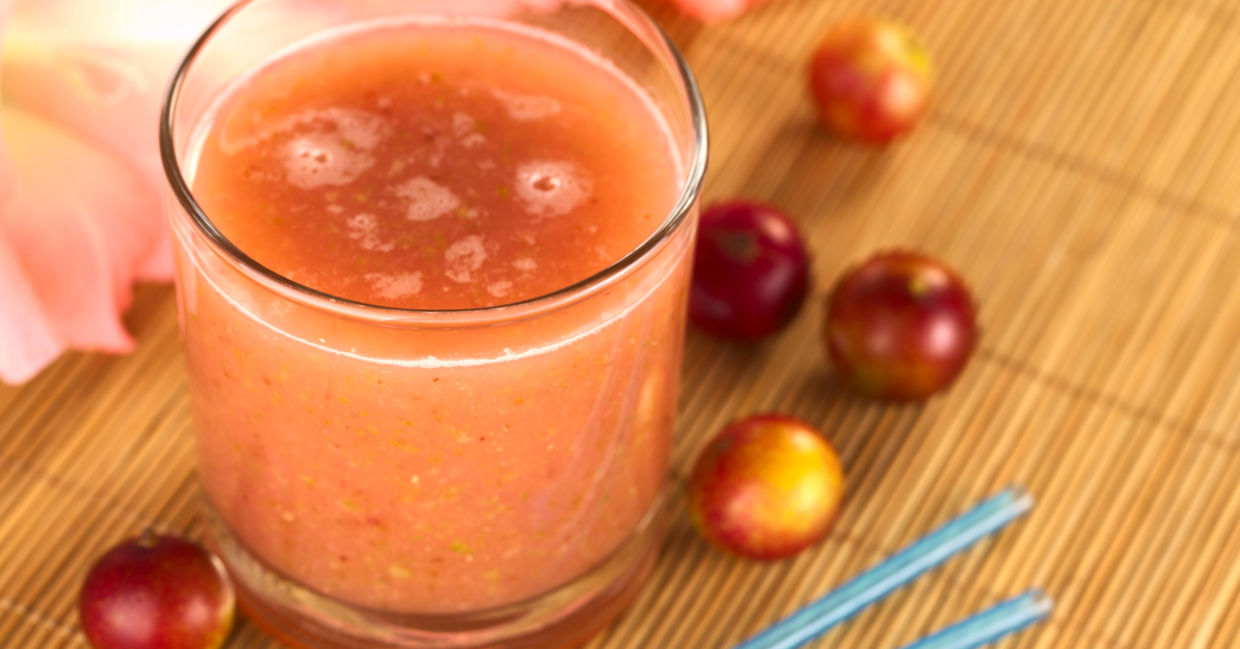 Camu camu berries beside a glass of freshly squeezed camu camu juice.