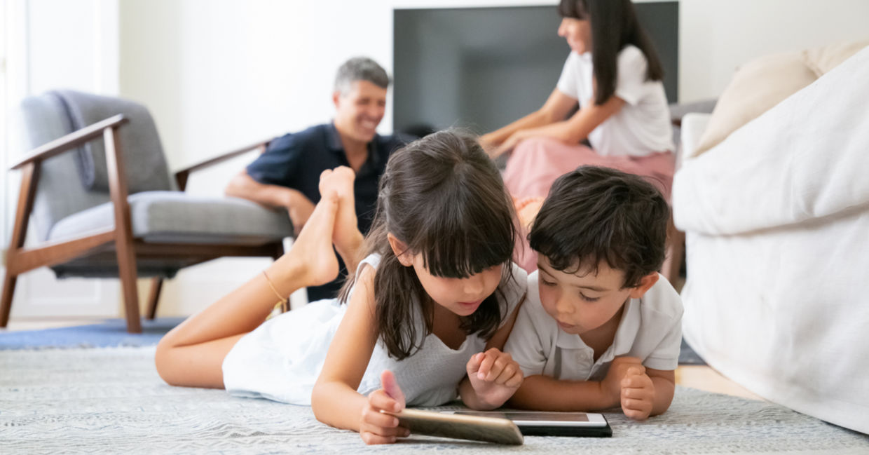 Cute kids lying on floor in living room and using digital gadgets