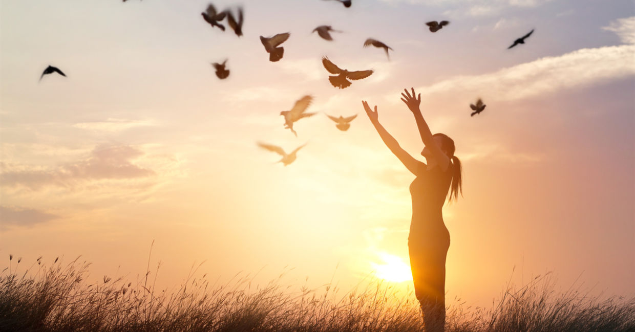 A symbol of letting go and forgiving: a woman’s arms are open wide while birds fly freely above.